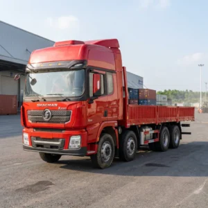 Shacman X3000 8x4 cargo truck, 12 wheels, red sleeper cab and 9.6 m drop-side cargo body, in a logistics yard