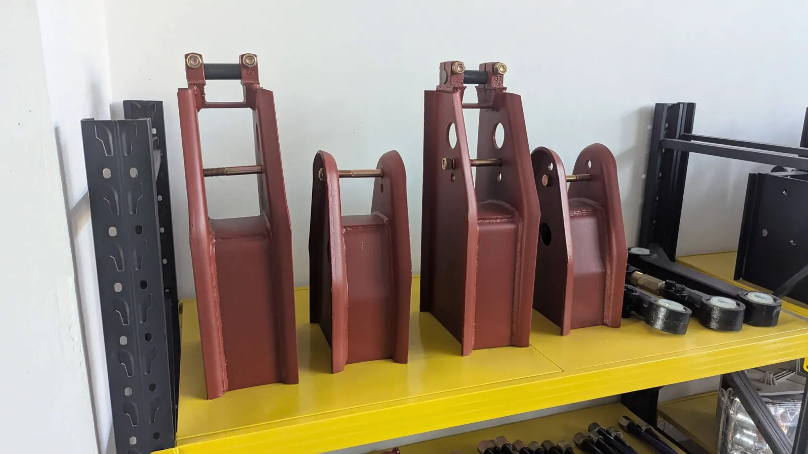 Red semi-trailer suspension hangers (tall front / rear and short middle hangers) and adjustable torque arms on a shelf